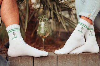 Füße, Glas mit Alkohol drin, Pflanze, Socken mit Schriftzug "Hugo"