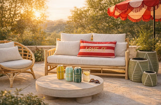 Terasse, Sonnenuntergang, Schirm, Sitzbank mit weißen Kissen, ein rotes Kissen, kleiner runder Tisch mit Vasen und Getränk