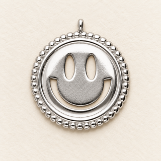 Silberfarbener runder Smiley-Charm aus Edelstahl mit ausgeschnittenen Augen, lächelndem Mund und perlenartigem Rand auf hellem Hintergrund.