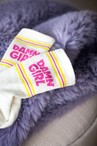 Sportsocken mit der Aufschrift Damn Girl in Gelb pink liegen auf einem Flieder farbenen Plüsch