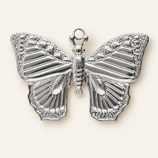 Silberner Schmetterling-Charm mit strukturierten Flügeln auf cremefarbenem Hintergrund.