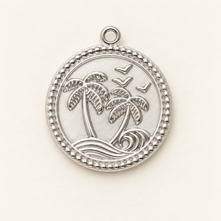 Runder silberner Charm mit zwei Palmen, Wellen und Vögeln auf cremefarbenem Hintergrund.