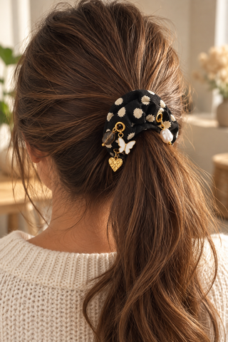 Scrunchie „Cream Dots“ mit cremefarbenen Tupfen und verschiedenen Charms, in einem braunen Pferdeschwanz getragen.