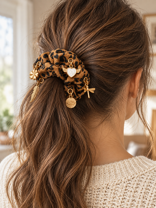 Scrunchie „Wild Leo“ im Leopardenmuster mit verschiedenen goldfarbenen Charms, in einem braunen Pferdeschwanz getragen\.