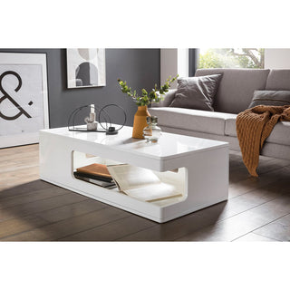 weißer couchtisch , grauer sofa, orangene vase mit grün, metallgegestände und transparentes gefäß, im hintergrund ein fenster und bilder