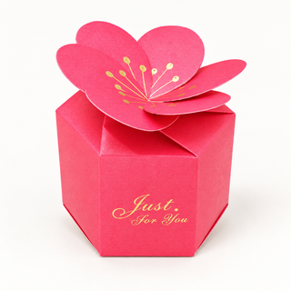 Fuchsiapinke Karton-Geschenkbox mit großer Papierblüte als Verschluss, goldenen Blütendetails und dem Schriftzug „Just for You“.