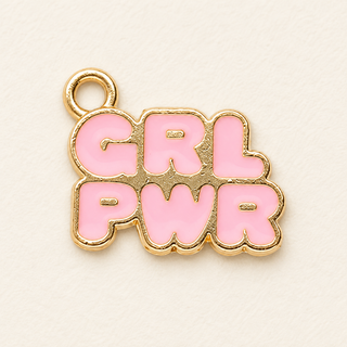 Charm mit hellrosa Schriftzug GRL PWR, goldfarbenen Konturen und Öse oben links auf hellem Hintergrund.