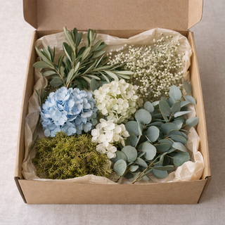 Karton mit verschiedenen Blumen wie eukalyptus, olivenzweige, schleierkraut hortensie weiß und blau und moos.Grauer Hintergrund