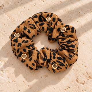 Scrunchie „Wild Leo“ im Leopardenmuster mit Kleeblatt\-, Feder\-, Libellen\-, Augen\- und geflügeltem Herzcharm auf beigem Travertin\.
