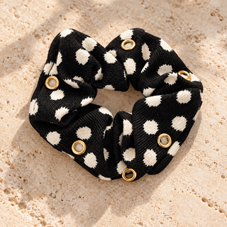 Schwarzer Scrunchie „Cream Dots“ mit cremefarbenen Tupfen und sechs goldfarbenen Ösen, ohne Charms auf beigem Travertin.