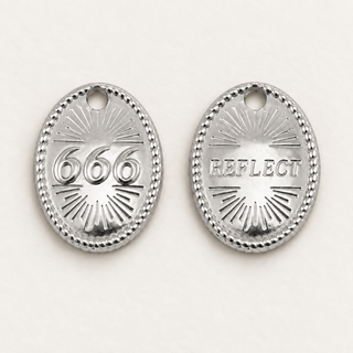 Silberner Engelszahlen-Charm 666 mit Rückseite REFLECT auf cremefarbenem Hintergrund.