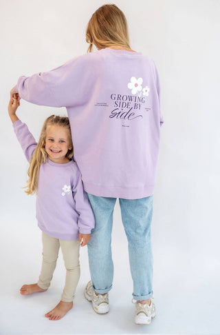 Mutter und Tochter in passenden Outfits lila farbene Pullover mit der Aufschrift Growing side by side und schönen weoßen Gänseblümchen 